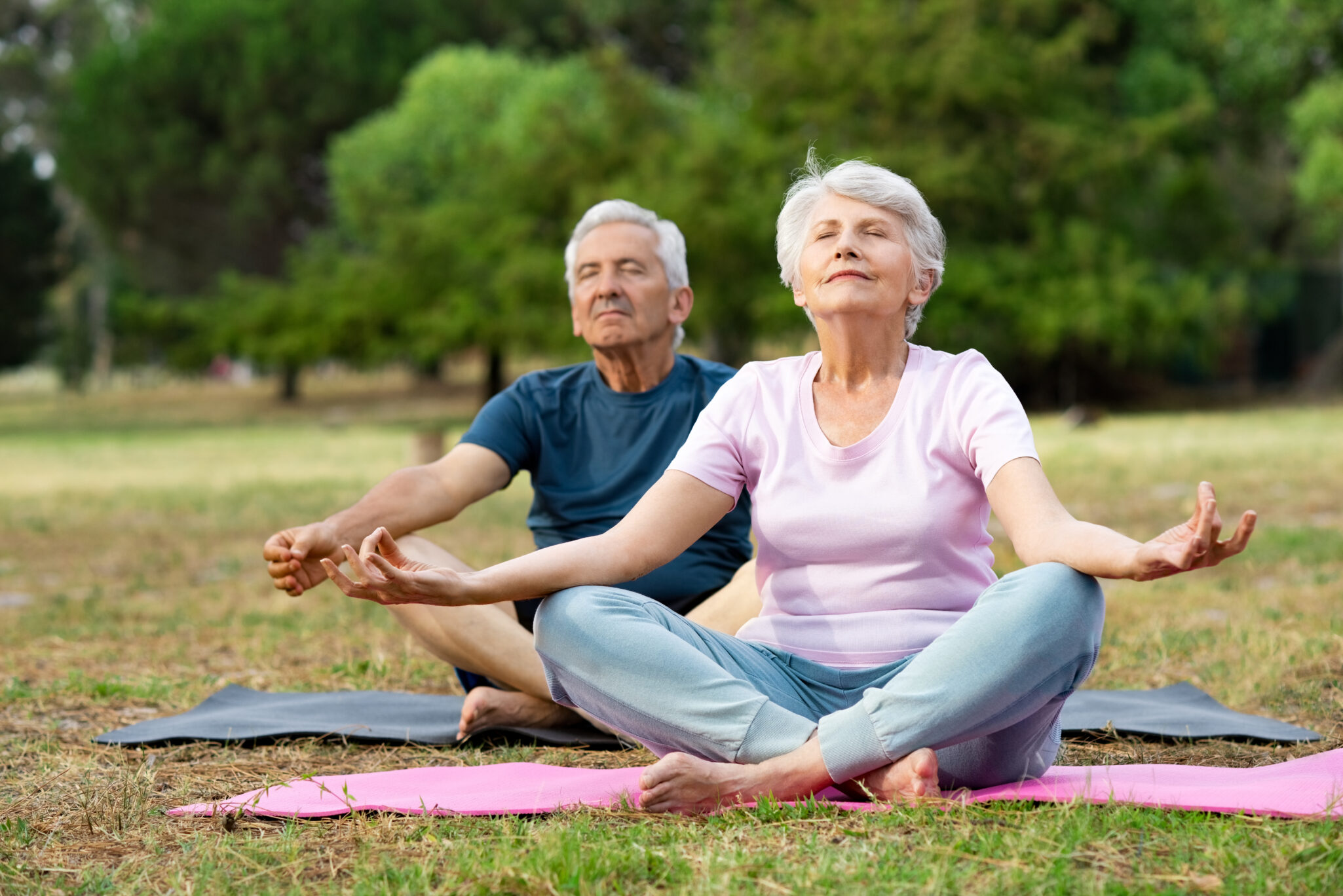 Senior man and elderly woman meditating sitting in lotus position at park with closed eyes.