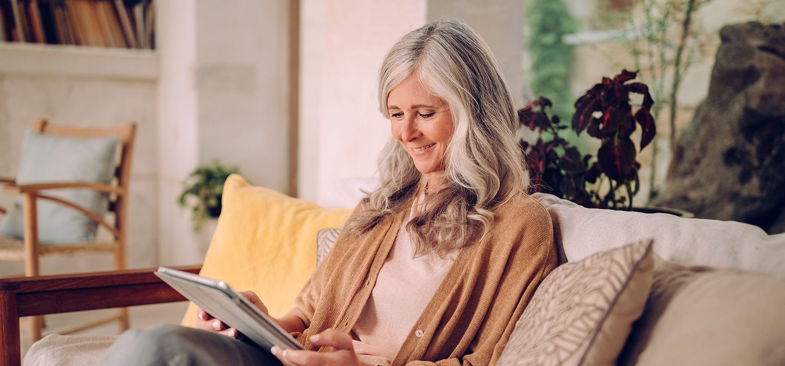 senior woman sitting on a couch smiling and looking at her tablet