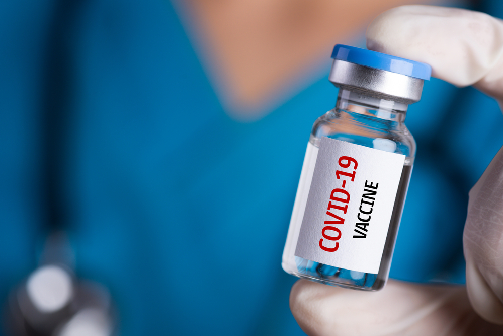 a nurse holding up a vial that says COVID-19 vaccine
