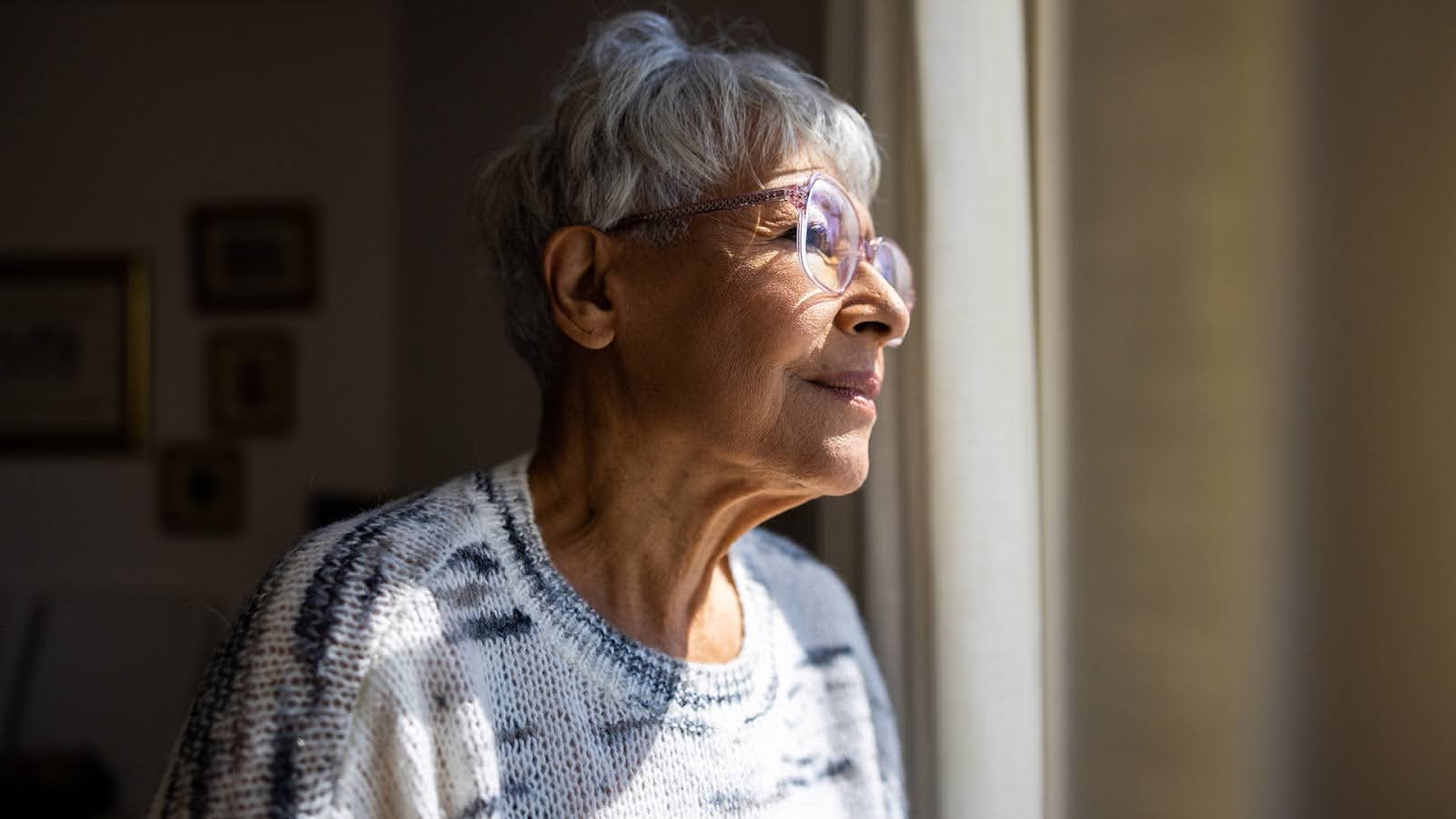Senior woman alone looking longingly out of a window