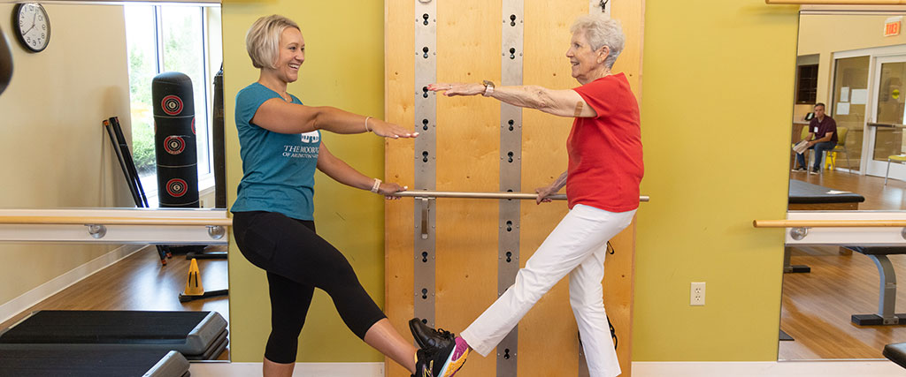 Senior woman working on balance in the fitness center with a trainer at The Moorings of Arlington Heights
