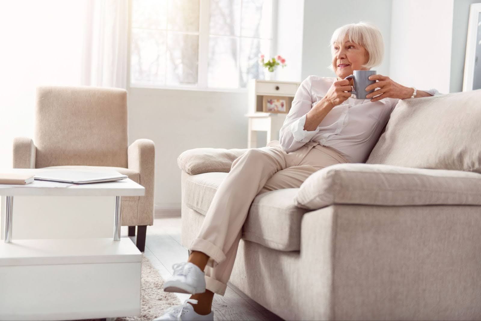 Senior woman sipping coffee on her sofa in her apartment at Ten Twenty Grove