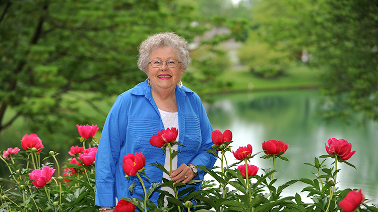 a senior woman posing with flowers in front of a body of water