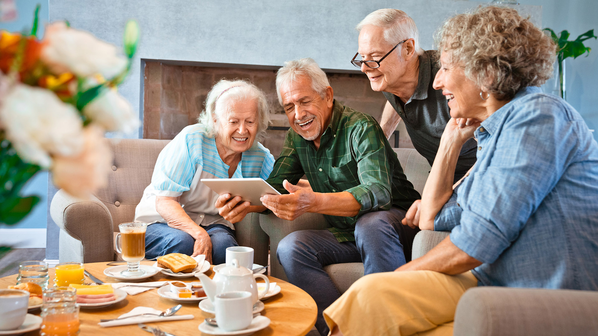 Smiling retired senior friends sharing digital tablet at nursing home.
