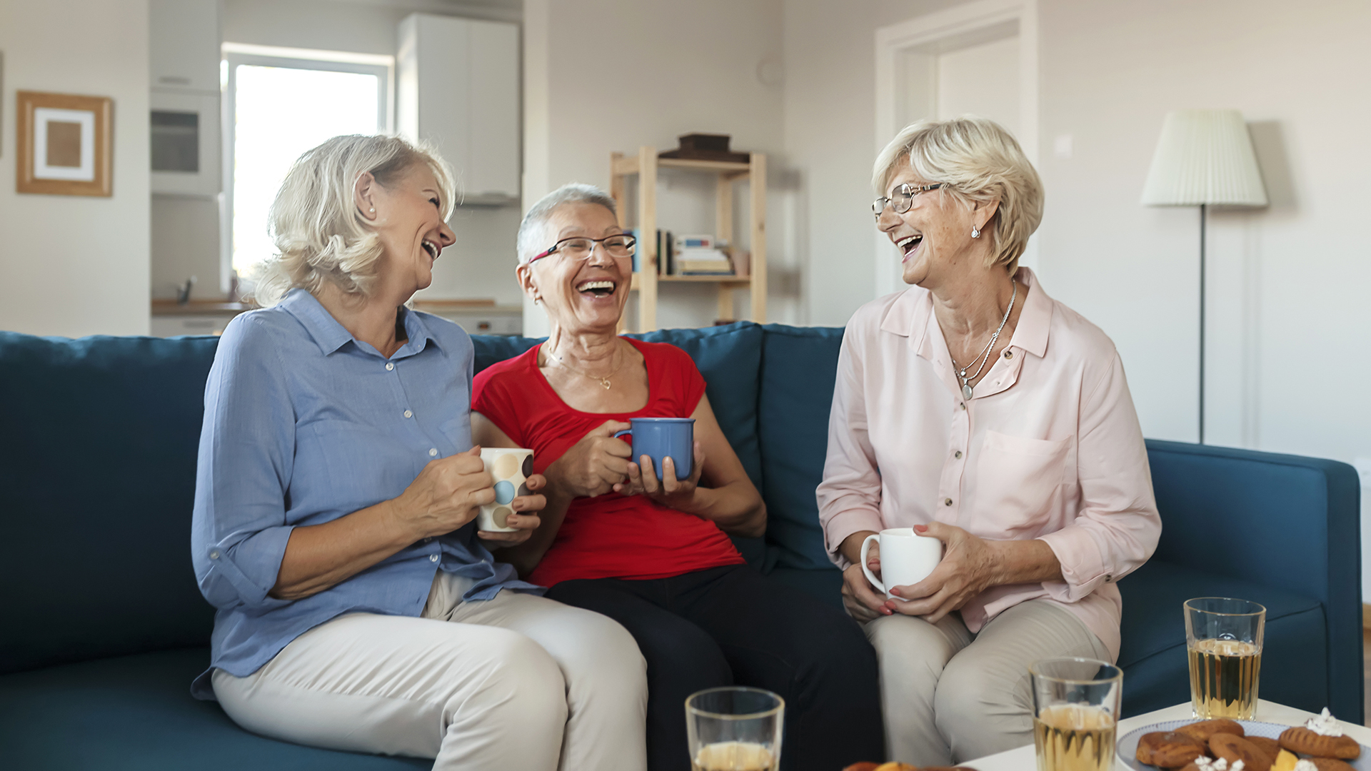 Three Female Seniors Drinking Coffee and Having Fun in the Living Room. Group of an Elderly Women Having Fun Talking and Laughing While Sitting on Sofa at Home