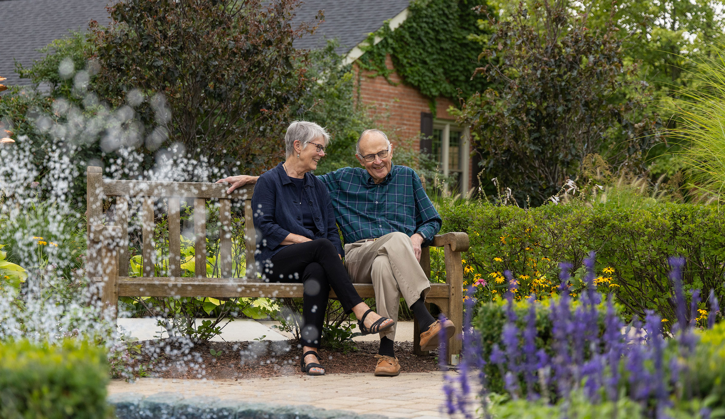 Senior couple sitting on a bench among the flowers in the courtyard at Westminster Place